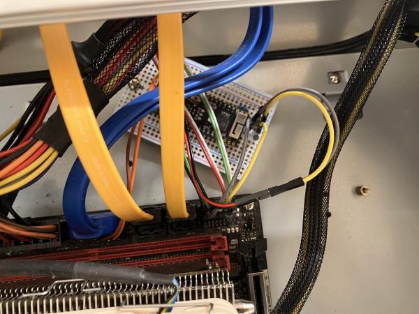 The inside of a PC case, where an ESP32 micro controller on an Adafruit Perma-Proto bread board is mounted inside the case and wired up to the mainboard with jumper wires for remote power control